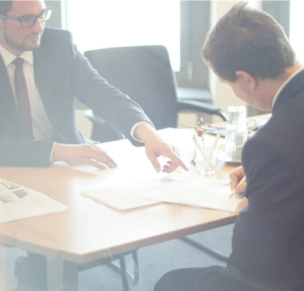 Zwei Personen an einem Schreibtisch, einer davon unterschreibt einen Vertag